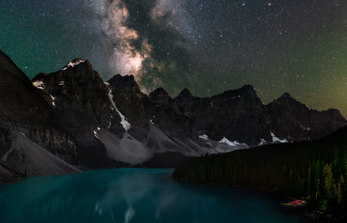 A night photograph of Moraine Lake, Alberta in Banff National Park. the milky way reflects in the pristine blue waters
