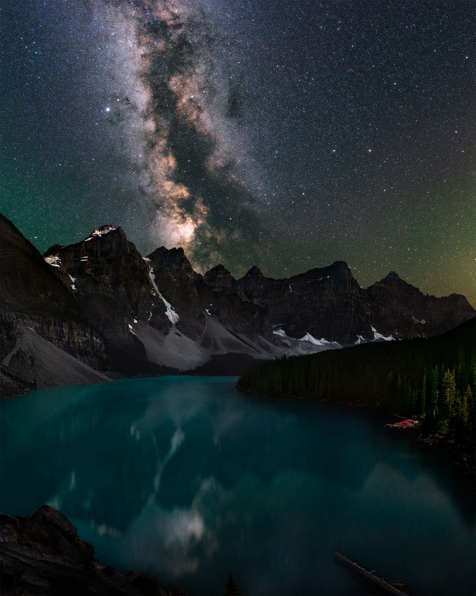 A night photograph of Moraine Lake, Alberta in Banff National Park. the milky way reflects in the pristine blue waters
