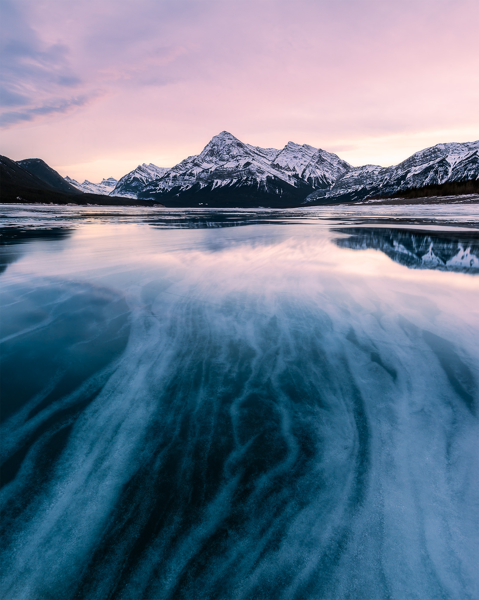 A frozen lake with interesting ice patterns leads to the mountains behind at Abraham Lake in Alberta