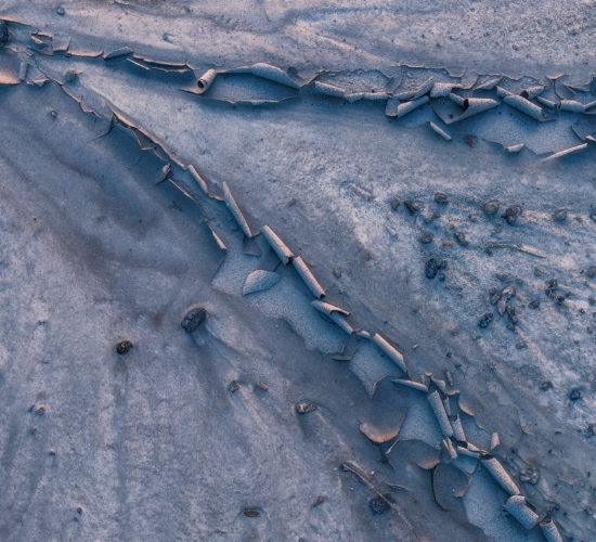 an intimate landscape photograph of cracked white clay reflecting sunset colours