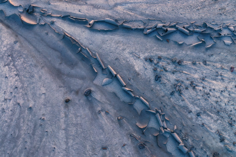 an intimate landscape photograph of cracked white clay reflecting sunset colours