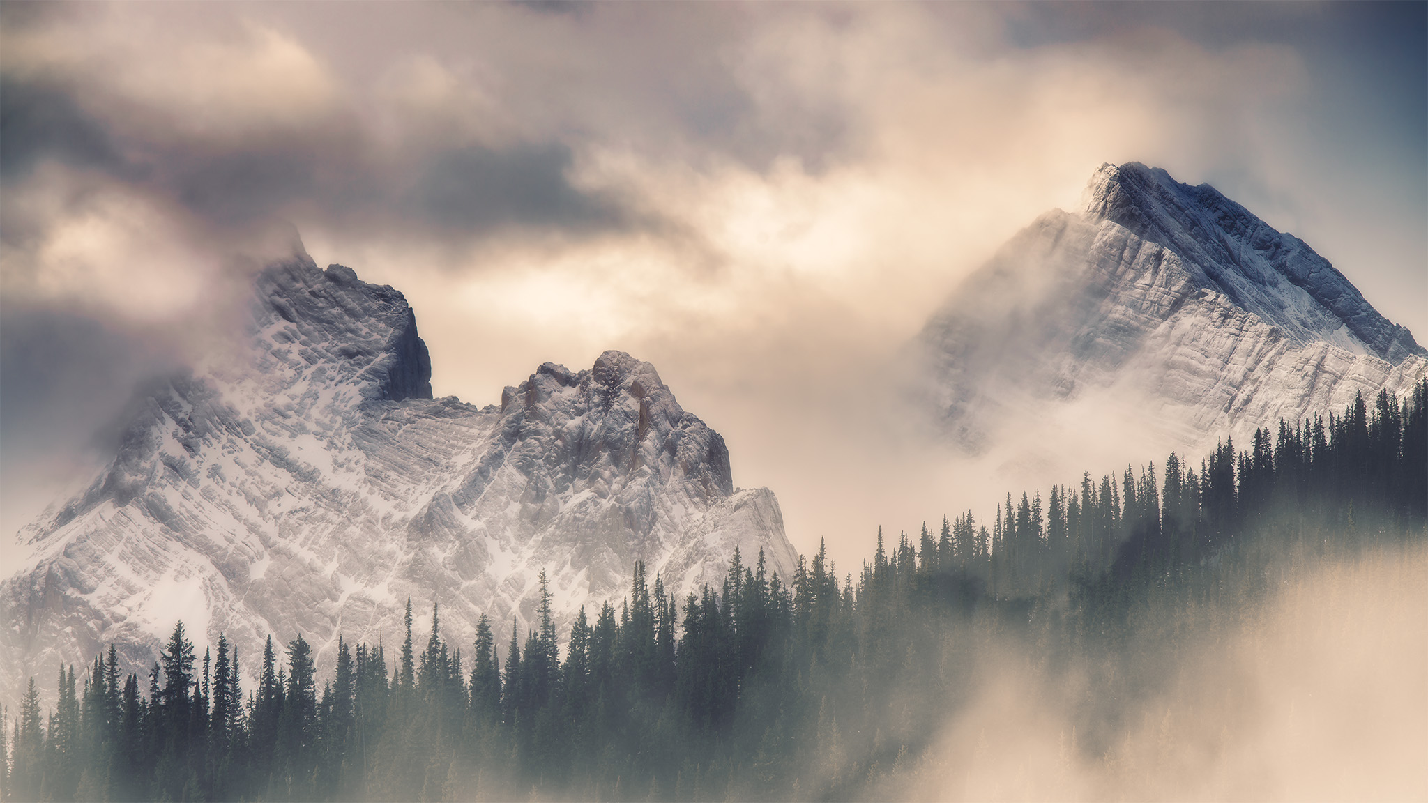 An intimate landscape photograph of two mountains surrounded in light and clouds in the Canadian Rockies