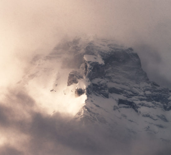 An intimate landscape photograph of a mountain peak surrounded by dramatic light and cloud in the Canadian Rockies