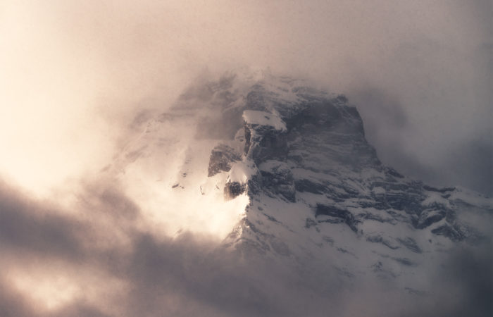 An intimate landscape photograph of a mountain peak surrounded by dramatic light and cloud in the Canadian Rockies