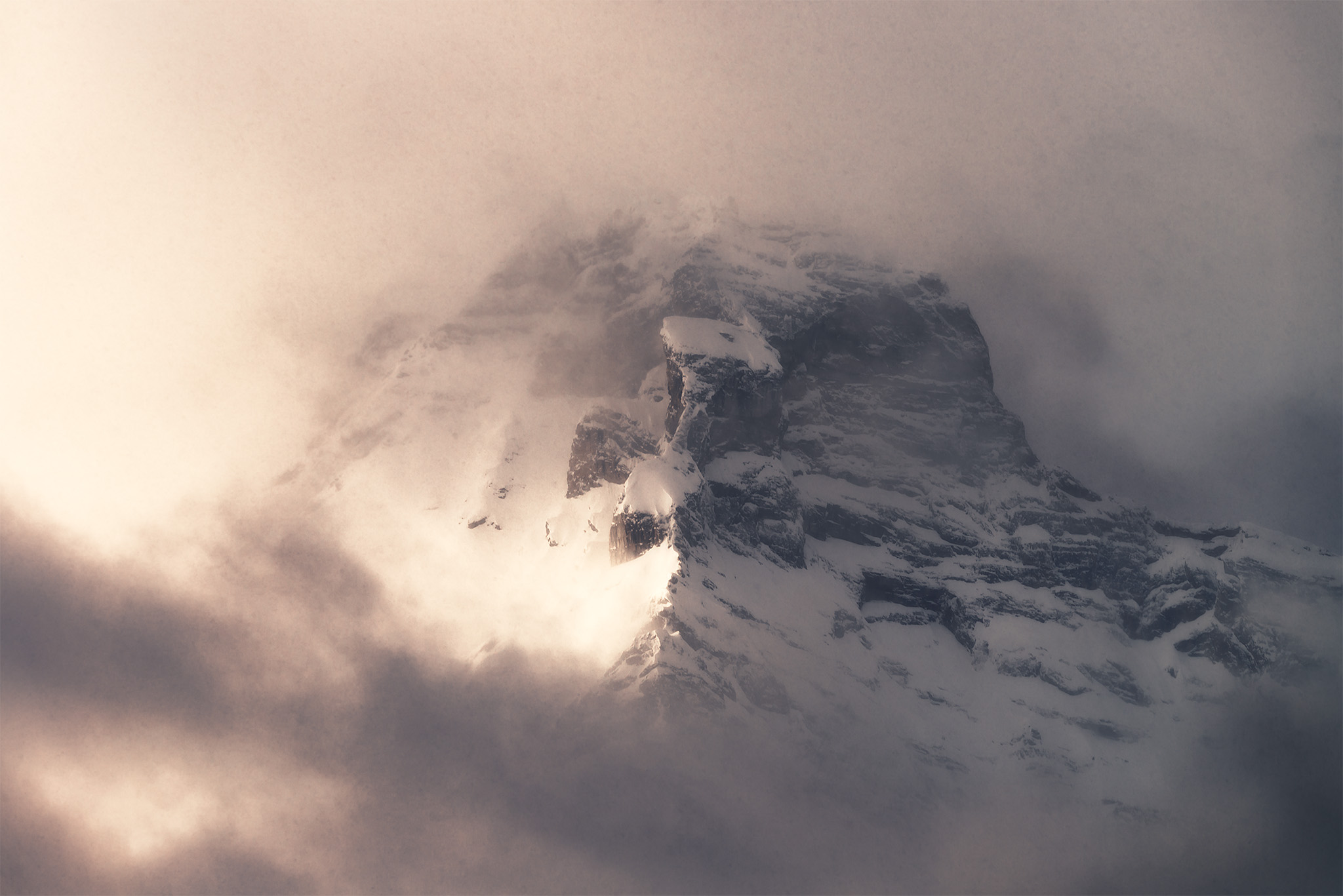 An intimate landscape photograph of a mountain peak surrounded by dramatic light and cloud in the Canadian Rockies
