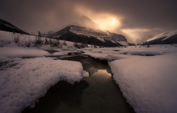 A landscape photograph of Tangle Ridge in Jasper National Park of the moon shining on a winter landscape