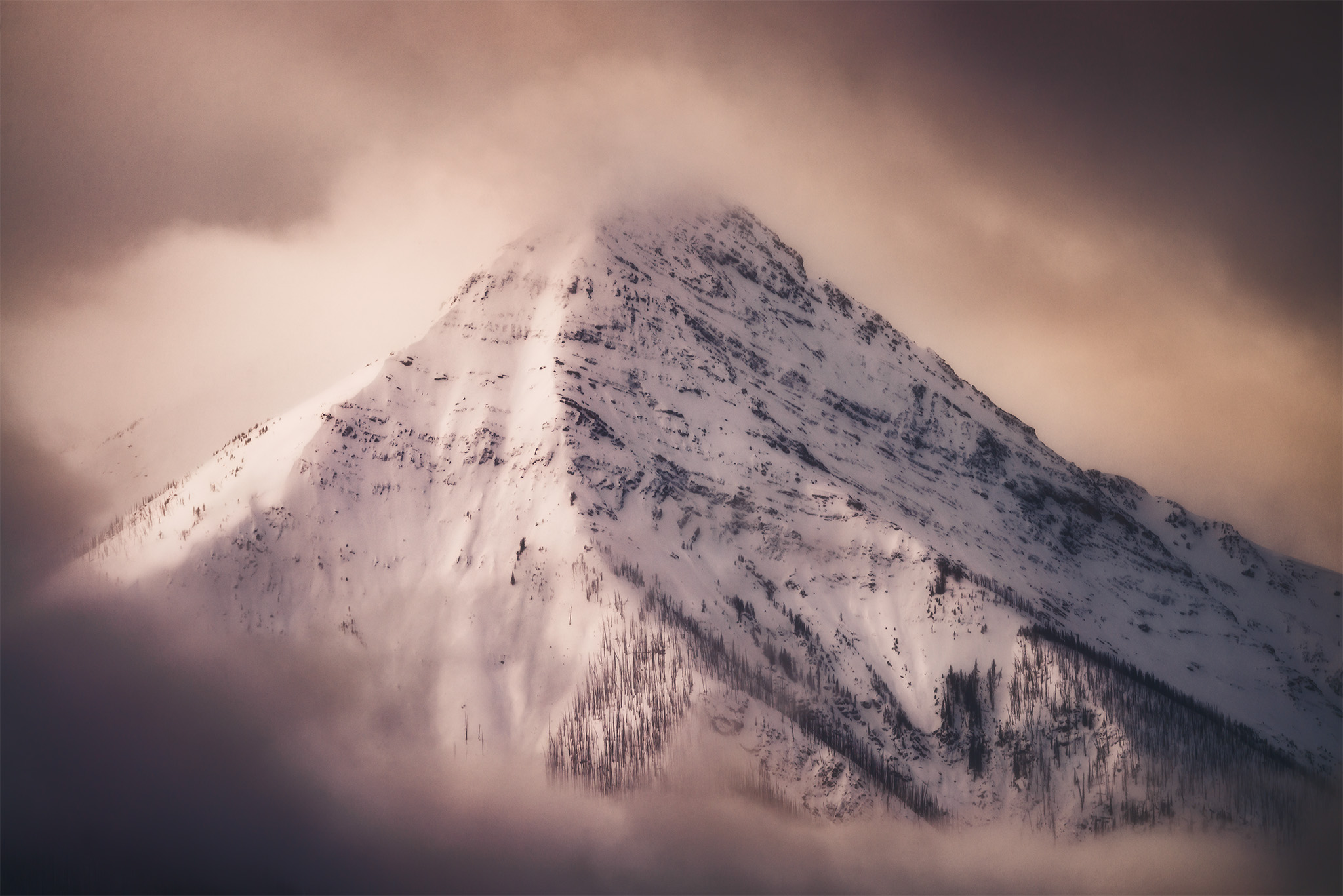 An intimate landscape of Vermilion Peak in Kootenay National Park shrouded by light and cloud in the winter