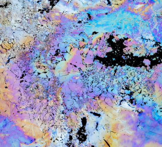 A intimate landscape photograph of the vibrant colours of natural oils in a pool of water