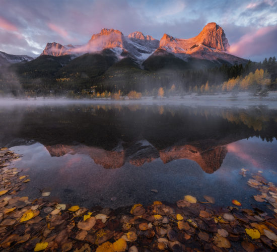 A landscape photograph of Quarry Lake near Canmore Alberta during a sunrise causing the mountain to glow red