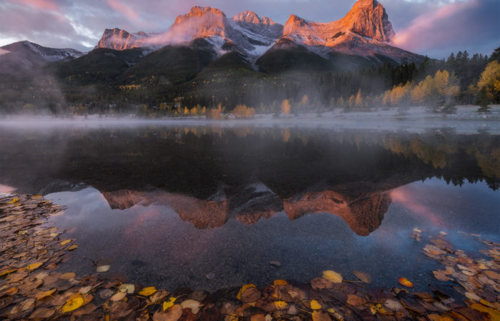 A landscape photograph of Quarry Lake near Canmore Alberta during a sunrise causing the mountain to glow red