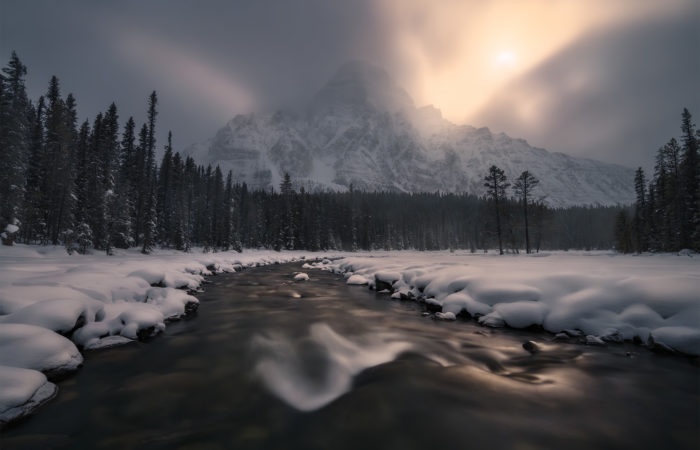 A landscape photograph of the moon setting beside Mount Chephren in Banff National Park